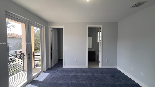 unfurnished bedroom featuring connected bathroom, dark colored carpet, a walk in closet, and access to outside