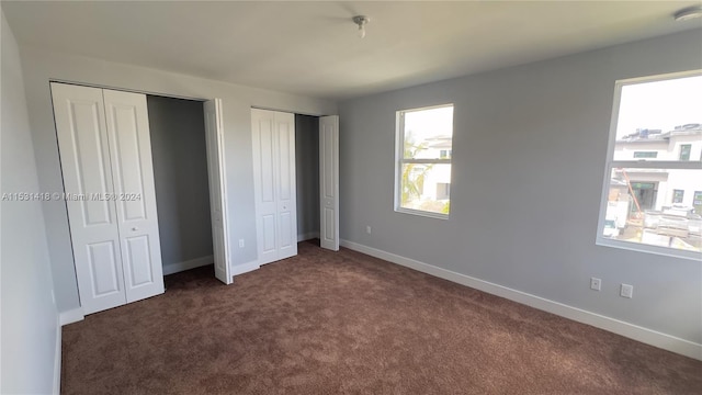 unfurnished bedroom featuring two closets, dark colored carpet, and multiple windows