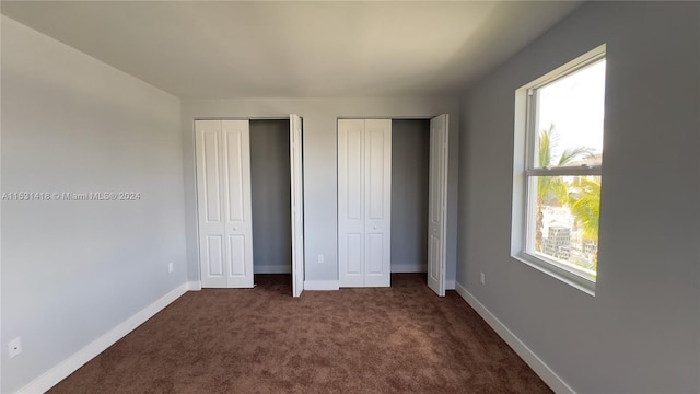 unfurnished bedroom featuring two closets and dark colored carpet