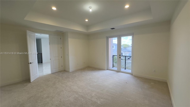 carpeted spare room with french doors and a raised ceiling