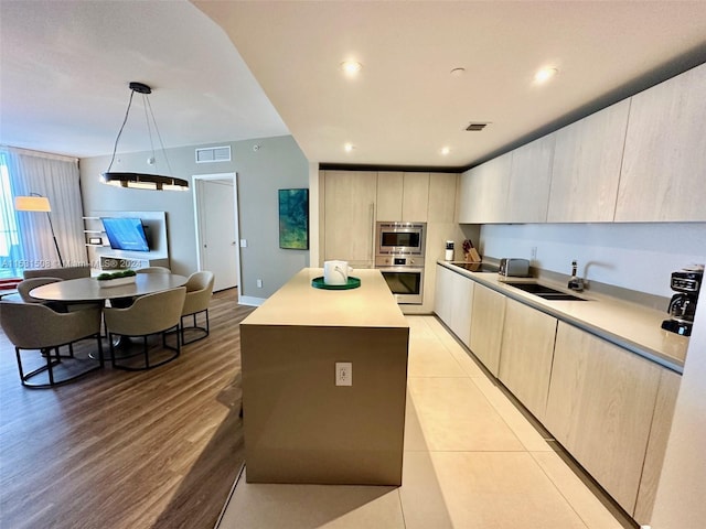 kitchen featuring decorative light fixtures, light hardwood / wood-style floors, sink, a center island, and light brown cabinetry