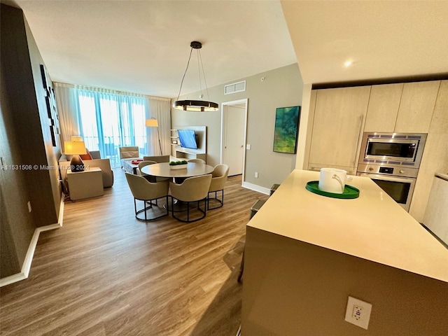 kitchen with hanging light fixtures, appliances with stainless steel finishes, light brown cabinetry, a kitchen island, and dark hardwood / wood-style flooring