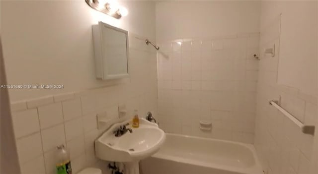 full bathroom with tile walls, tiled shower / bath combo, toilet, sink, and tasteful backsplash