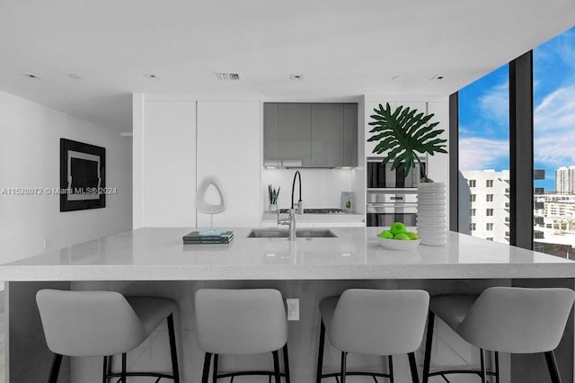 kitchen featuring sink, gray cabinetry, a breakfast bar, light stone countertops, and stainless steel oven