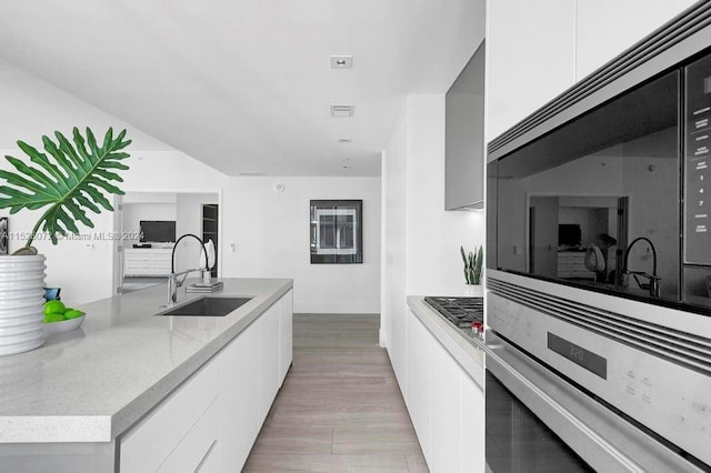 kitchen featuring light stone countertops, white cabinetry, appliances with stainless steel finishes, sink, and light wood-type flooring