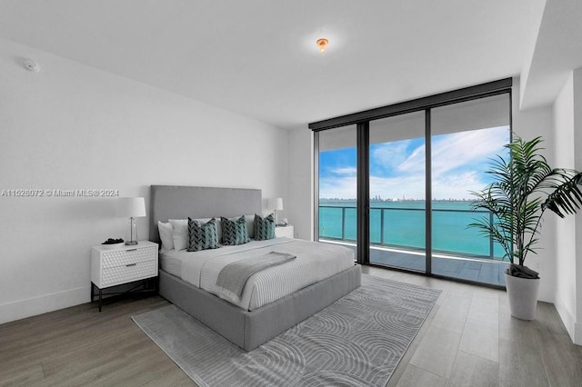 bedroom featuring a water view, access to exterior, wood-type flooring, and a wall of windows