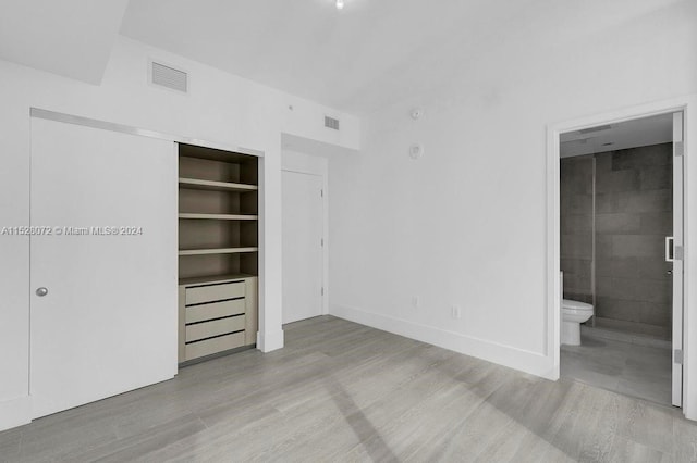 unfurnished bedroom with ensuite bathroom and light wood-type flooring