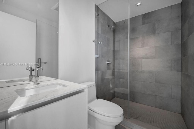 bathroom with toilet, a tile shower, and vanity