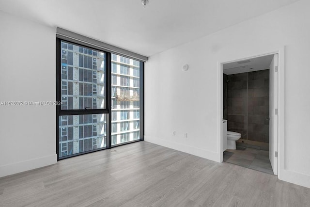 empty room with a wall of windows and light hardwood / wood-style flooring