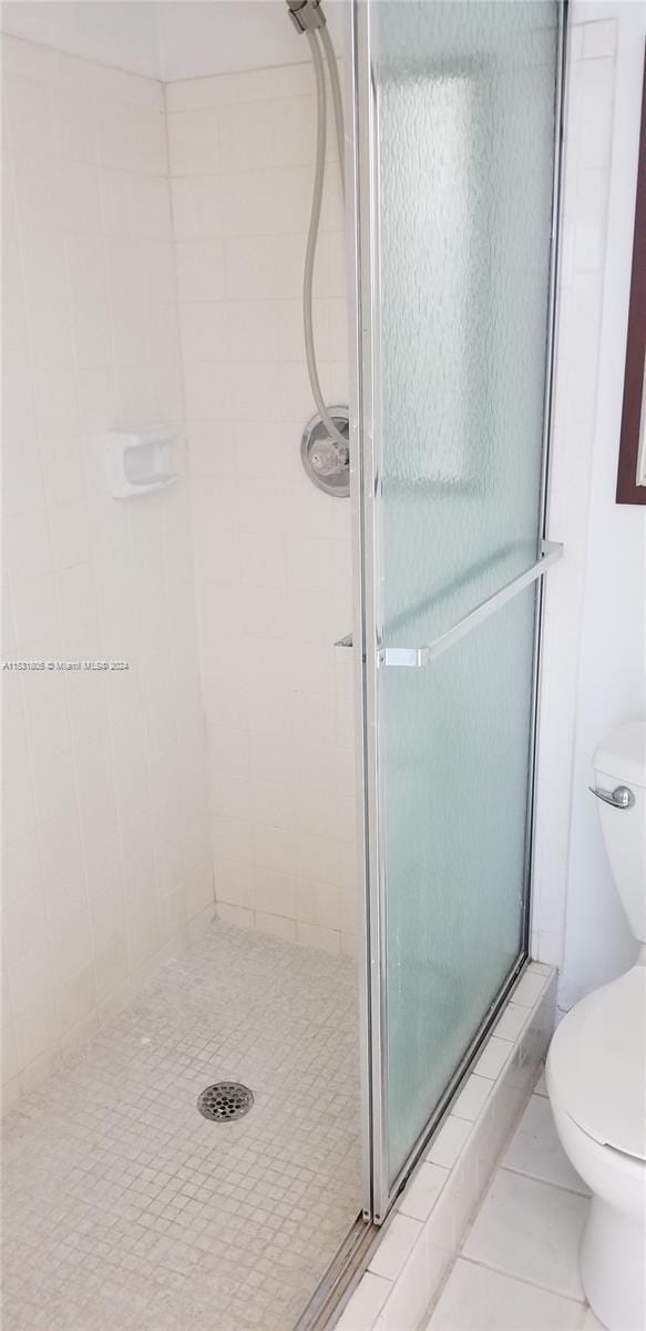 bathroom with a shower with door, tile floors, and toilet