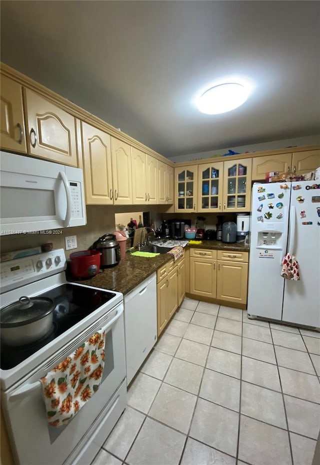 kitchen with light brown cabinetry, white appliances, sink, light tile floors, and dark stone counters