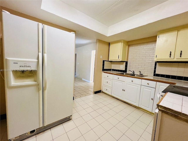 kitchen featuring tile counters, white fridge with ice dispenser, sink, backsplash, and light tile patterned floors