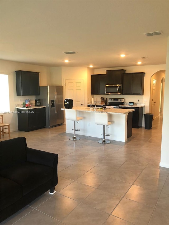 kitchen with light tile floors, an island with sink, a breakfast bar area, and stainless steel appliances