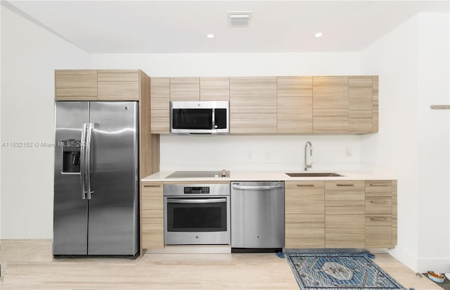 kitchen with stainless steel appliances, sink, and light hardwood / wood-style flooring