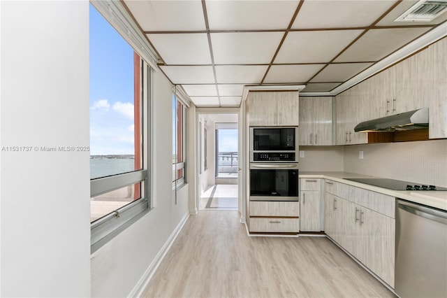 kitchen featuring light brown cabinetry, light wood-type flooring, backsplash, black appliances, and a water view