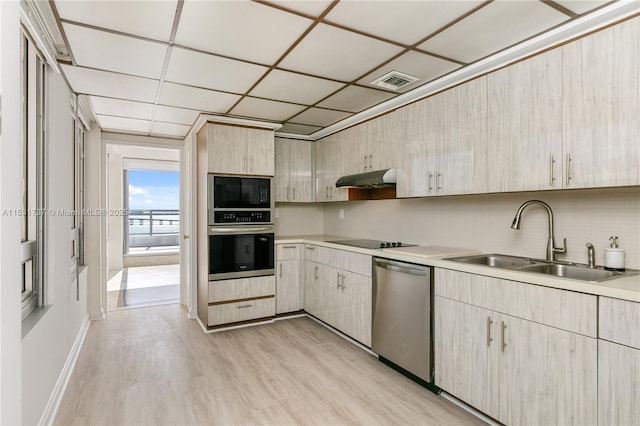 kitchen featuring a drop ceiling, sink, black appliances, light brown cabinets, and light hardwood / wood-style floors