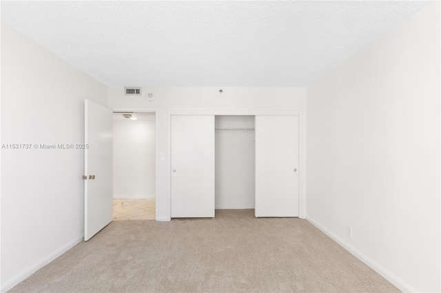 unfurnished bedroom featuring light carpet, a textured ceiling, and a closet