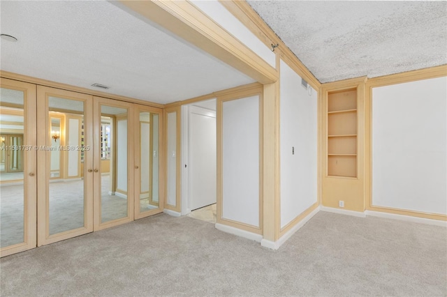 empty room with built in shelves, light carpet, and ornamental molding