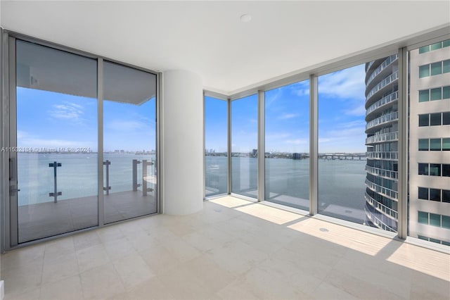 spare room with a water view, a wall of windows, light tile floors, and a wealth of natural light