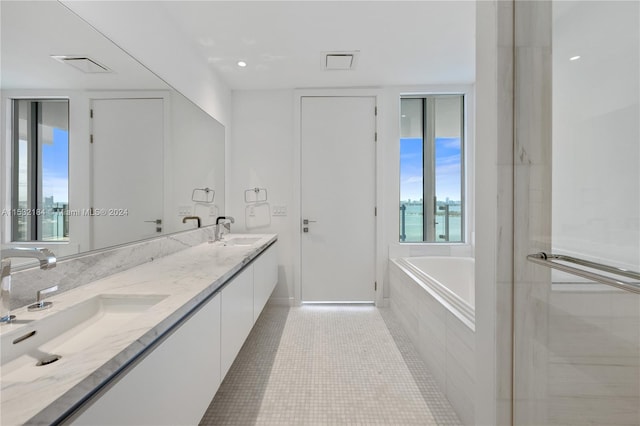 bathroom featuring tiled tub, dual vanity, and tile flooring