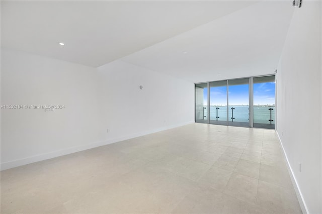 empty room featuring expansive windows, light tile flooring, and a water view