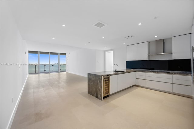 kitchen with floor to ceiling windows, white cabinets, light tile flooring, wine cooler, and wall chimney exhaust hood