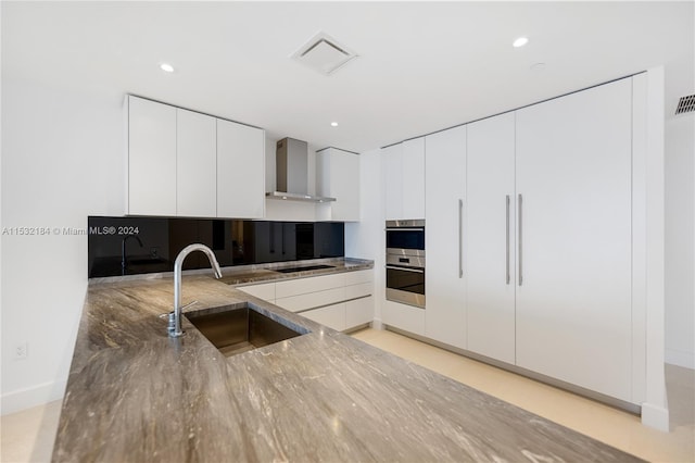 kitchen featuring black electric cooktop, white cabinetry, wall chimney exhaust hood, stainless steel double oven, and sink