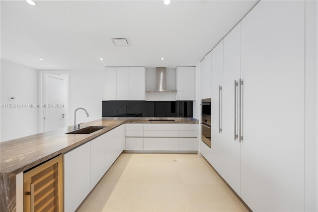 kitchen featuring white cabinets, beverage cooler, sink, and wall chimney range hood