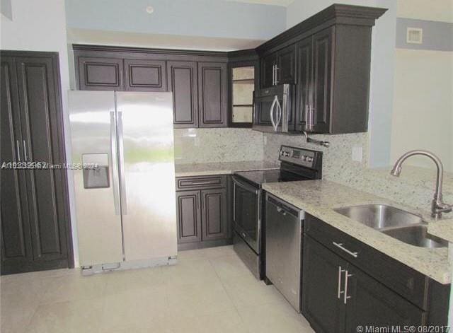 kitchen featuring dark brown cabinetry, light stone counters, light tile floors, sink, and stainless steel appliances