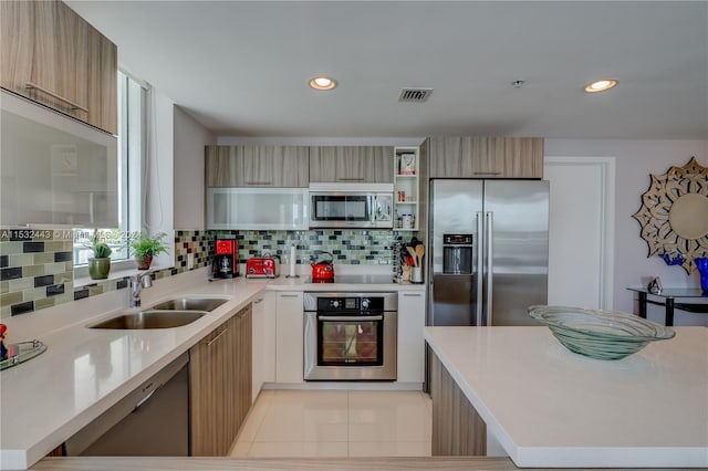 kitchen featuring light brown cabinets, light tile floors, appliances with stainless steel finishes, backsplash, and sink