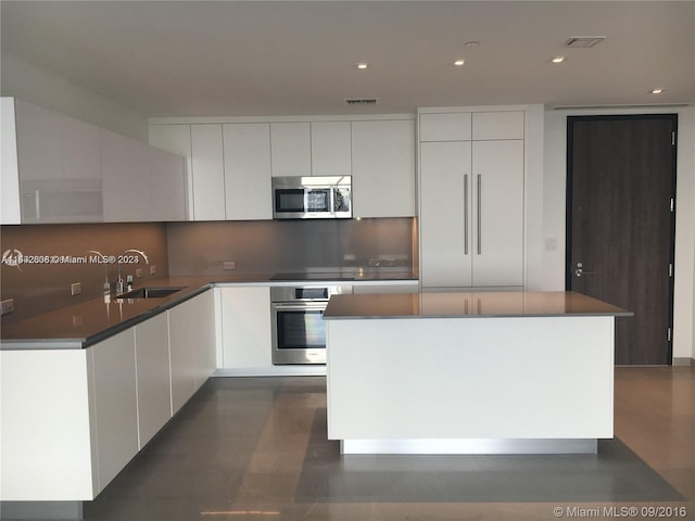 kitchen with backsplash, stainless steel appliances, white cabinetry, and a center island