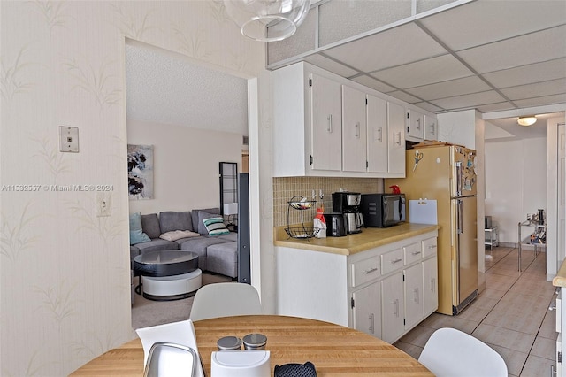 kitchen featuring white cabinetry, backsplash, high end refrigerator, a paneled ceiling, and light tile floors