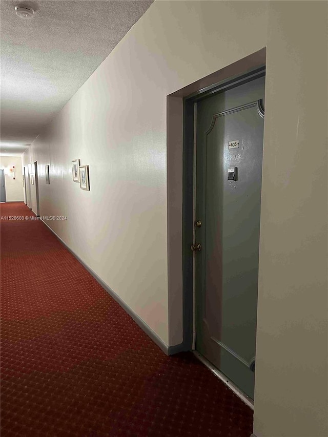 corridor with a textured ceiling and dark carpet