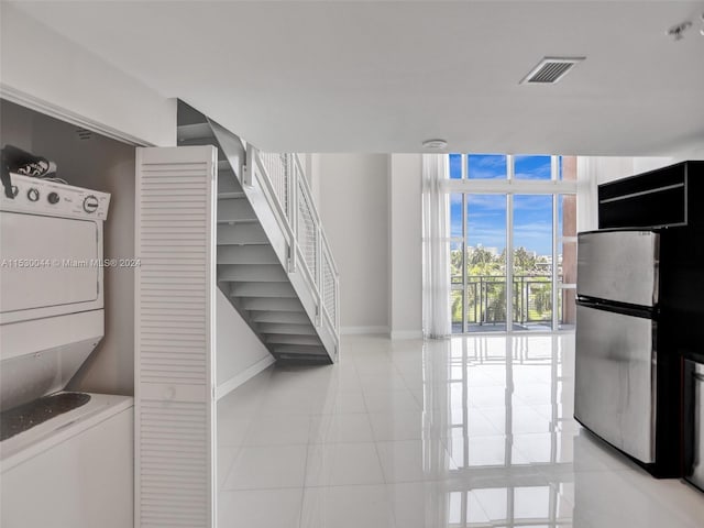 interior space featuring stacked washing maching and dryer, stainless steel refrigerator, and light tile flooring