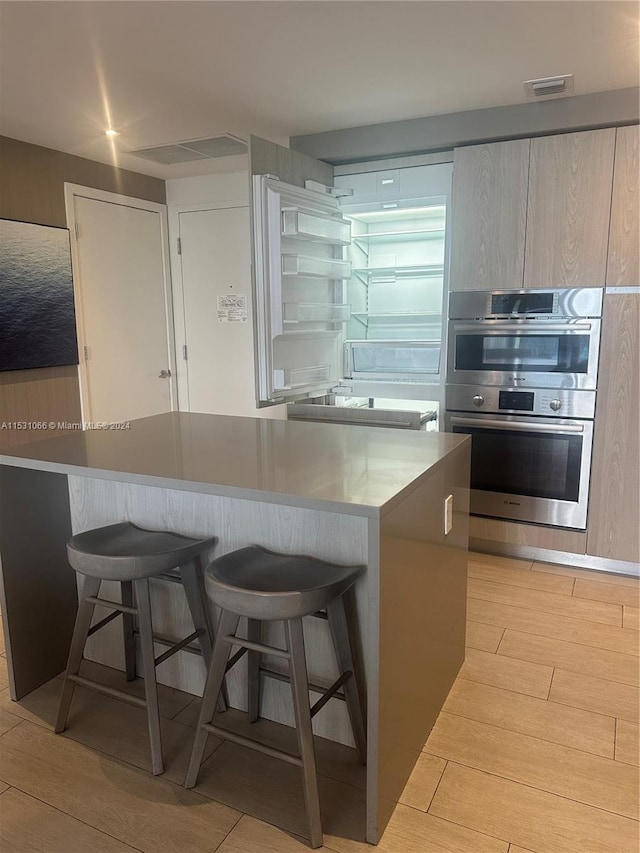 kitchen with a kitchen breakfast bar, a kitchen island, light hardwood / wood-style floors, and double oven