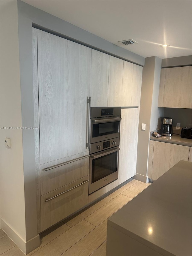 kitchen featuring stainless steel double oven, light brown cabinetry, and light wood-type flooring