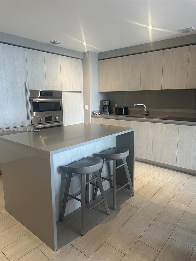 kitchen featuring double oven, a kitchen bar, sink, light wood-type flooring, and a center island