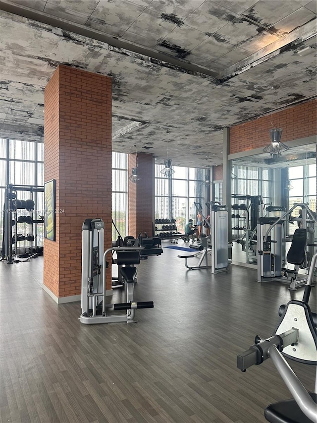 exercise room with brick wall, a wall of windows, ceiling fan, and dark hardwood / wood-style floors