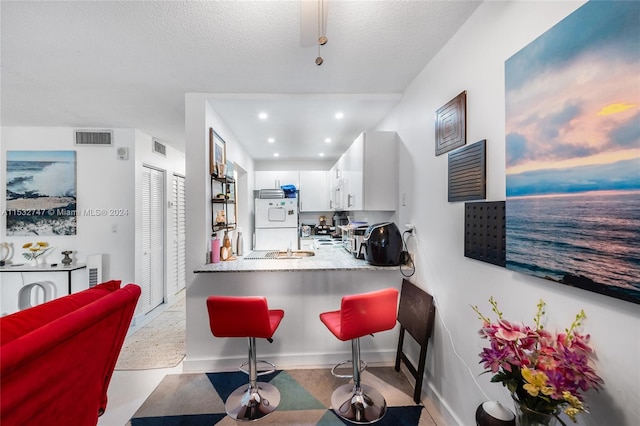 kitchen with white appliances, a breakfast bar, a textured ceiling, white cabinets, and kitchen peninsula