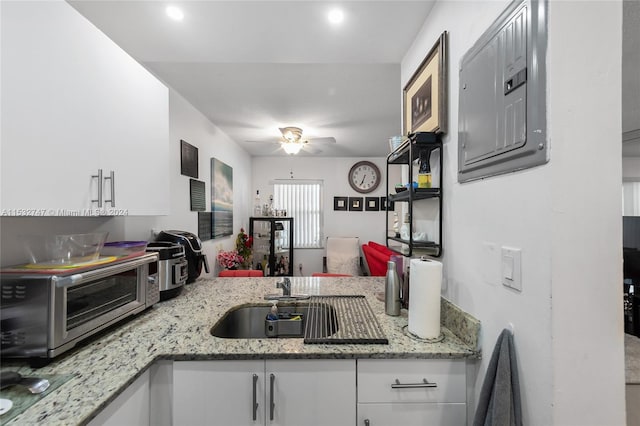 kitchen with sink, light stone counters, electric panel, ceiling fan, and white cabinets