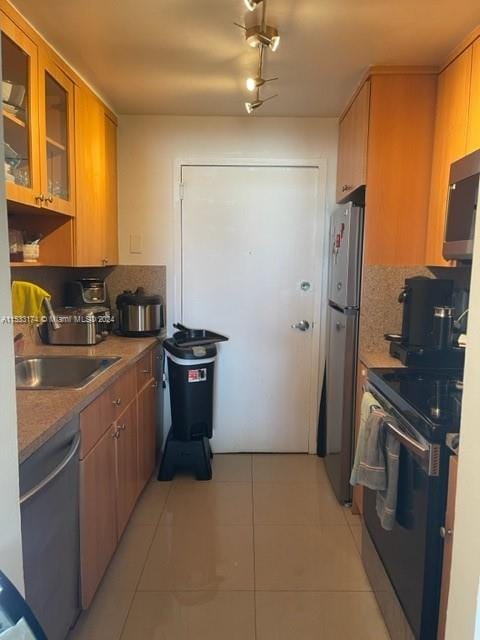 kitchen featuring sink, light tile floors, rail lighting, appliances with stainless steel finishes, and backsplash