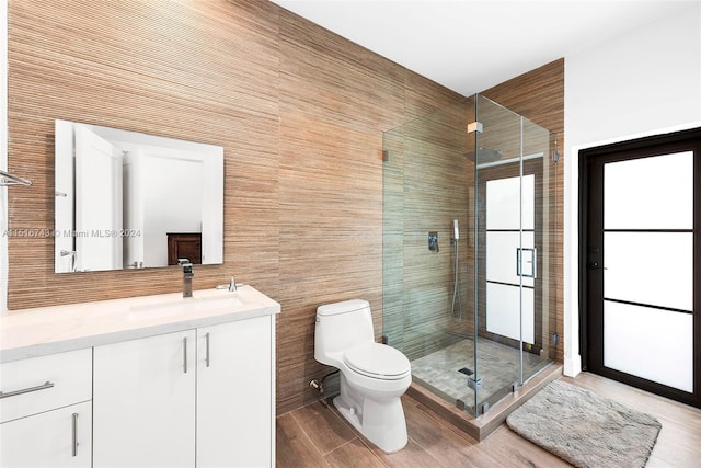 bathroom featuring toilet, an enclosed shower, vanity, wood-type flooring, and tile walls