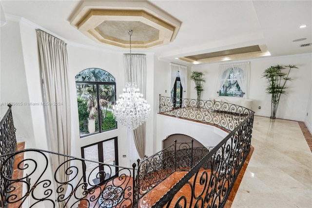 hallway with a chandelier, a tray ceiling, light tile flooring, and ornamental molding