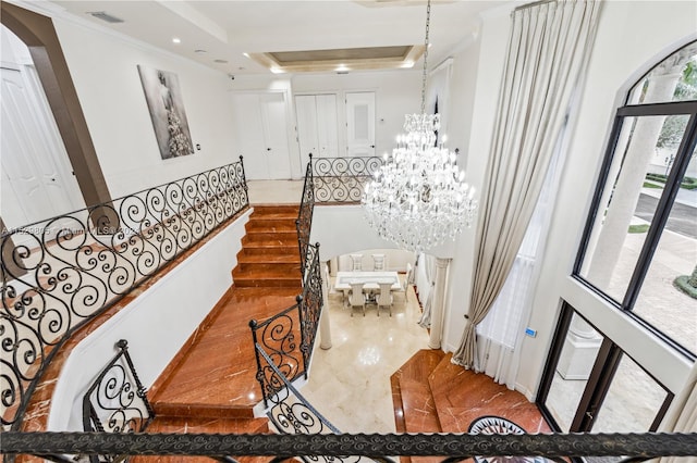 stairway featuring a tray ceiling, light tile floors, a chandelier, a towering ceiling, and ornamental molding