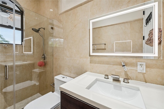 bathroom featuring a shower with shower door, vanity with extensive cabinet space, toilet, and tile walls