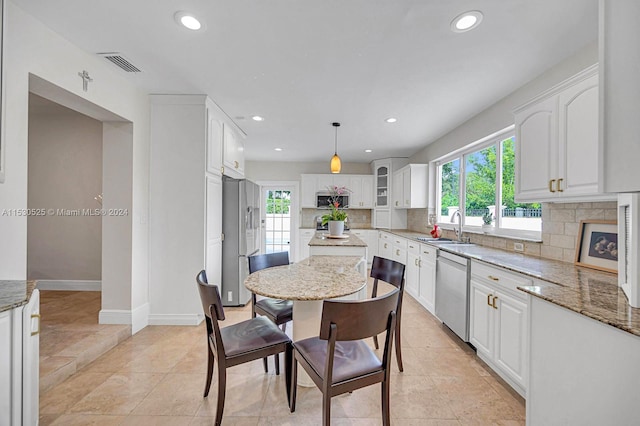 kitchen featuring white cabinetry, backsplash, stainless steel appliances, light stone counters, and decorative light fixtures