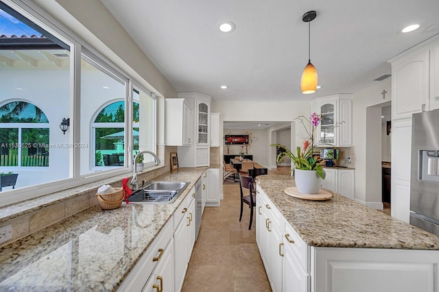 kitchen with pendant lighting, sink, a center island, light stone counters, and white cabinets