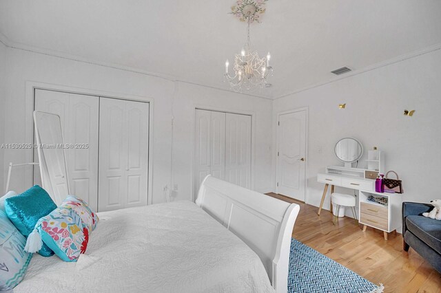 bedroom with an inviting chandelier, crown molding, a fireplace, and light hardwood / wood-style floors