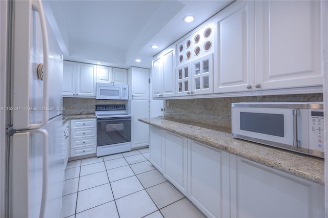 kitchen featuring white appliances, light tile patterned flooring, backsplash, and white cabinetry