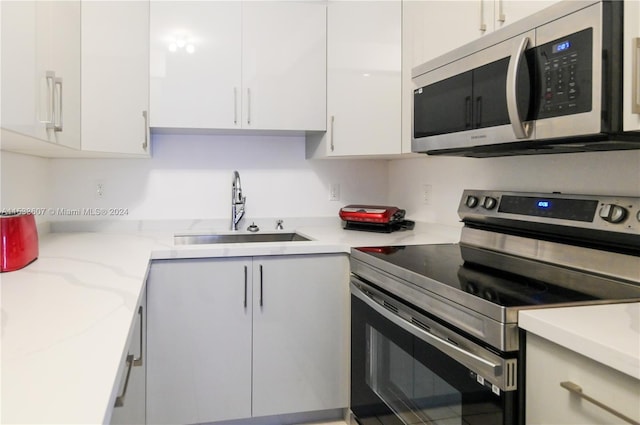 kitchen featuring white cabinetry, appliances with stainless steel finishes, light stone countertops, and sink